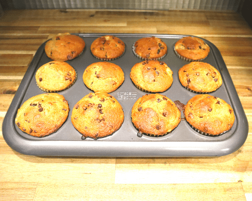 A tray of baked banana chocolate chip muffins right out of the oven they are made from fresh milled flour