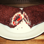 chocolate swiss cake roll sliced in half showing the cream and fresh strawberries inside