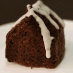 close up of a gingerbread muffin shaped like a house with a white sugar glaze poured on the roof to look like snow on the roof