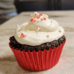 close up of a chocolate peppermint sourdough cupcake with cream cheese buttercream topped with candy cane sprinkles in a red foil cupcake wrapper