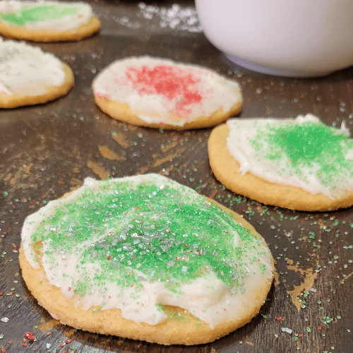close up of a cut out cookie with green and silver sprinkles other cookies in the background
