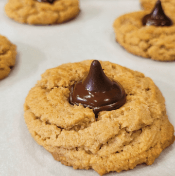 close up of a peanut butter spelt cookie with a dark chocolate kiss candy melted onto the top
