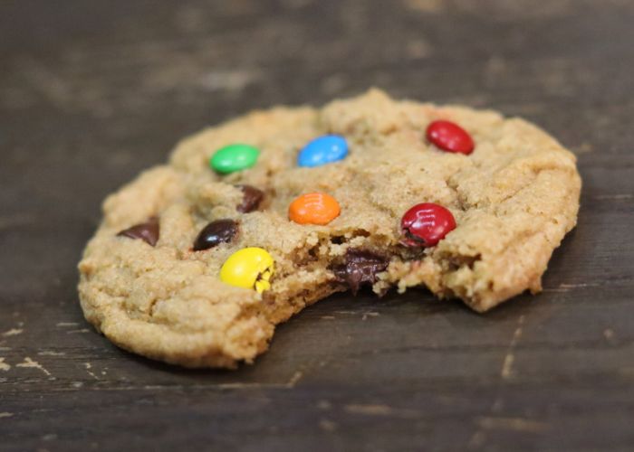 close up of a single sourdough cookie with a bite out of it showing the chocolate chips and m&m candies