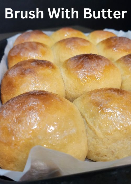 close up of a tray of baked whole wheat hawaiian rolls brushed with butter, making them shiny