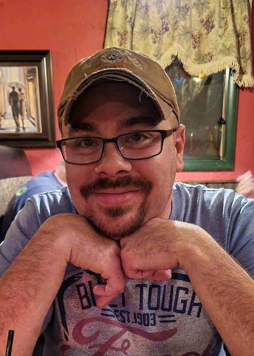 photo of a man wearing a baseball hat, leaning on both hands under his chin.