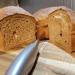 two whole wheat loaves of bread and a bread knife, one loaf is sliced in half exposing the inside texture of both halves of bread. how to make sandwich bread without eggs