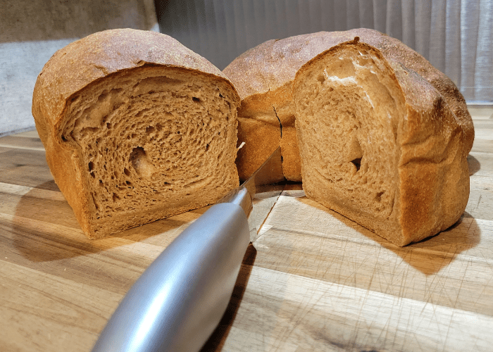 two whole wheat loaves of bread and a bread knife, one loaf is sliced in half exposing the inside texture of both halves of bread. how to make sandwich bread without eggs