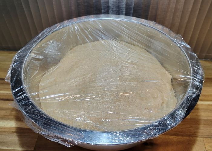 a metal bowl of risen eggless bread dough waiting to be punched down