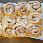 a baking tray of warm homemade whole wheat cinnamon rolls made with fresh dates with a sugar glaze on top