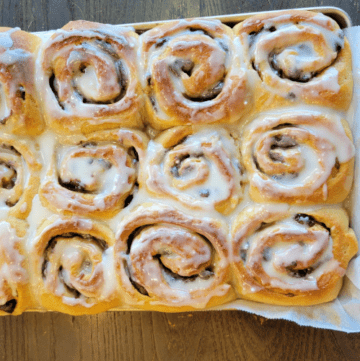 a baking tray of warm homemade whole wheat cinnamon rolls made with fresh dates with a sugar glaze on top