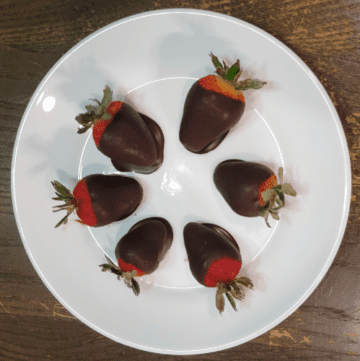 white circle plate on a wooden table with six dark chocolate dipped fresh strawberries