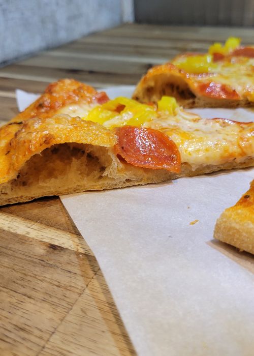 a pizza slice showing a big air pocket in the edge of a pepperoni & banana pepper pizza made with fresh milled flour