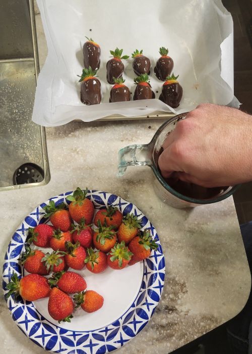 hand dipping fresh strawberry in dark chocolate