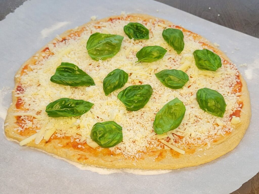 homemade fresh milled flour pizza dough topped with fresh basil ready to be baked