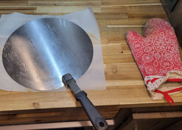 a metal pizza peel next to a red oven mit