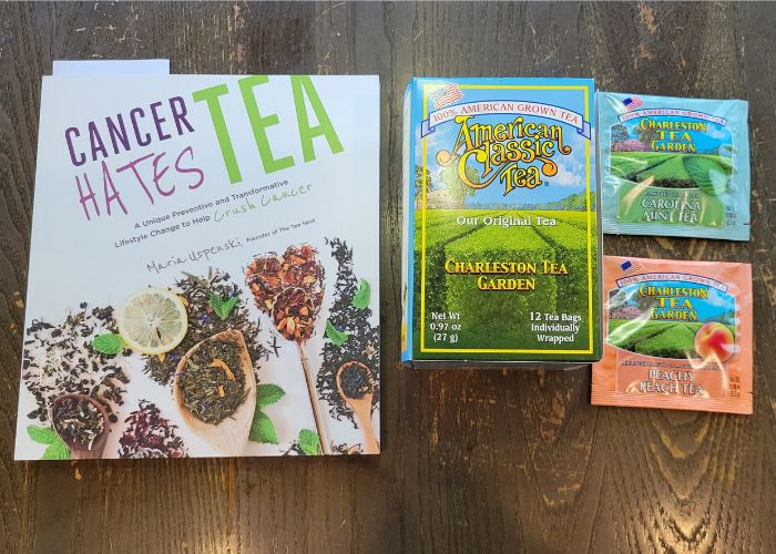 a Book that reads, "Cancer Hates Tea," a box of Charleston Tea Company Black Tea, a packet of Peach Tea, and a Packet of Mint Tea.