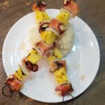 baked Chicken bacon pineapple onion skewers on a white plate criss-crossed over a pile of white rice