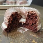 a close up of a glazed chocolate donut made with fresh milled flour, it has a bite out of it, showing the inside texture.