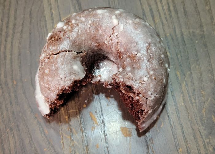 arial close up of a bitten glazed chocolate cake donut sitting on a table