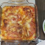 arial photo of a table scape with a homemade baked Manicotti with marinara sauce from scratch, white plates, bread, and salad, and easy croutons