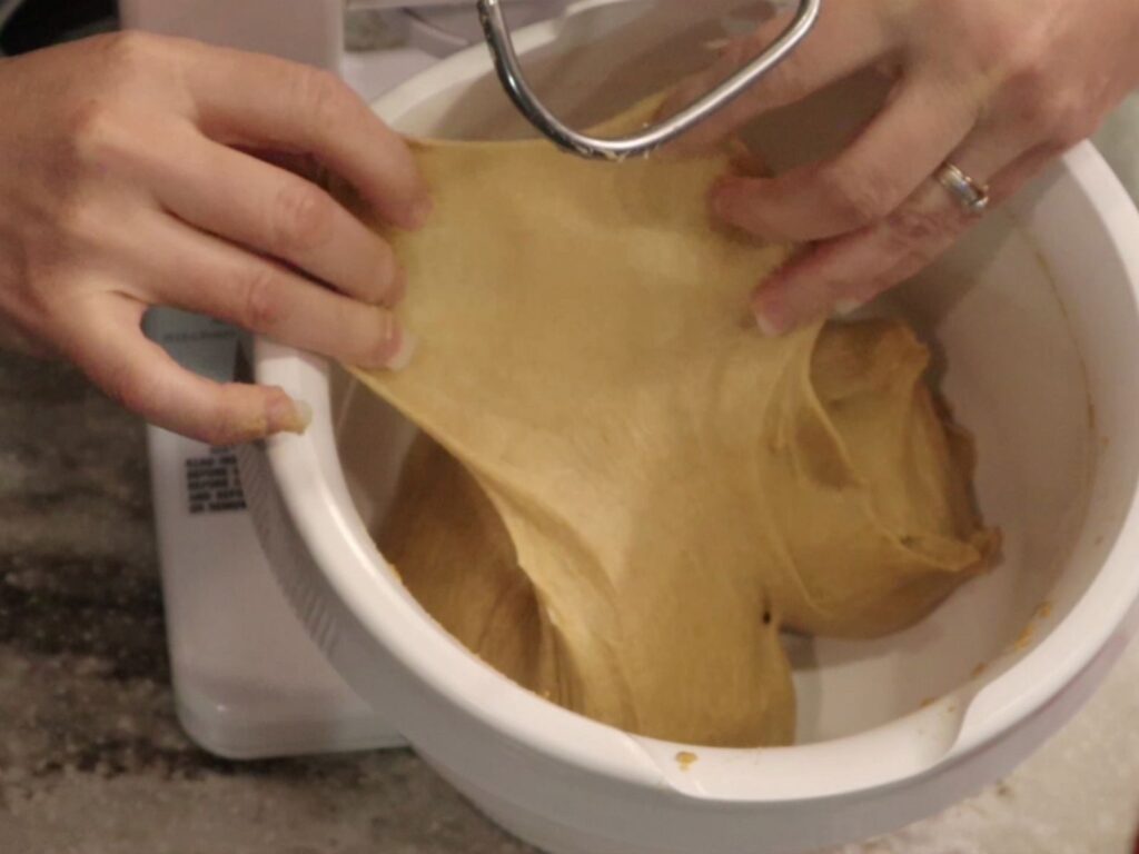 hands stretching bread dough to get a successful window pane test