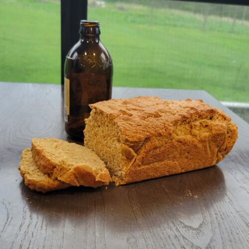 a sliced loaf of freshly milled flour beer bread with an empty amber beer bottle next to it.