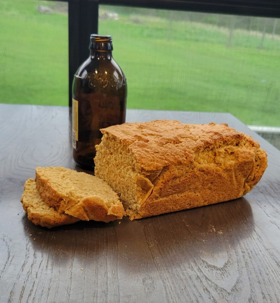 a sliced loaf of freshly milled flour beer bread with an empty amber beer bottle next to it.