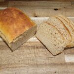 a loaf of Kamut yeast bread sliced in half with slices next to the rest of the loaf sitting on a wooden countertop