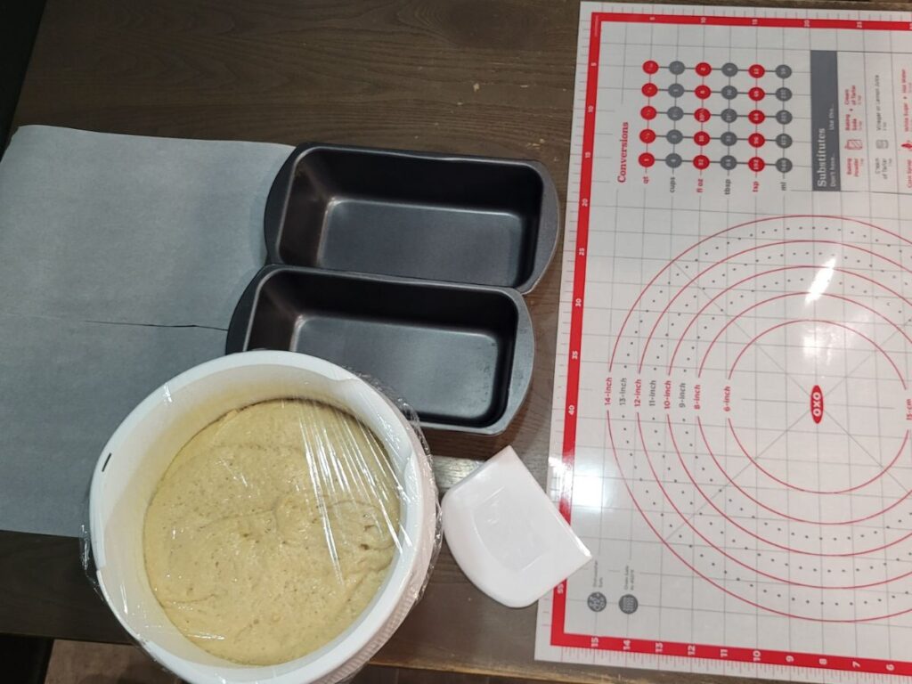 dough in a bowl next to 2 loaf tins and a rolling pastry mat.