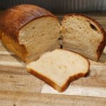 a loaf of homemade fresh milled flour sandwich bread sliced in half with one slice laying in front of the loaf.