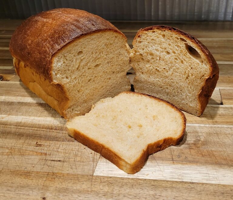 a loaf of homemade fresh milled flour sandwich bread sliced in half with one slice laying in front of the loaf.