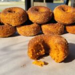 a double row of baked pumpkin spice cake donuts made with fresh milled flour with one in front with a bite our of it.