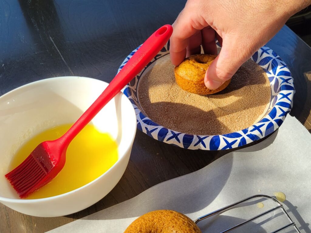 hands rolling pumpkin donuts in pumpkin spice sugar coating