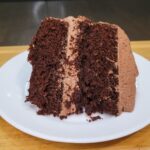 A slice of Chocolate Cake Made With Fresh Milled Flour iced with chocolate buttercream sitting on a white plate.