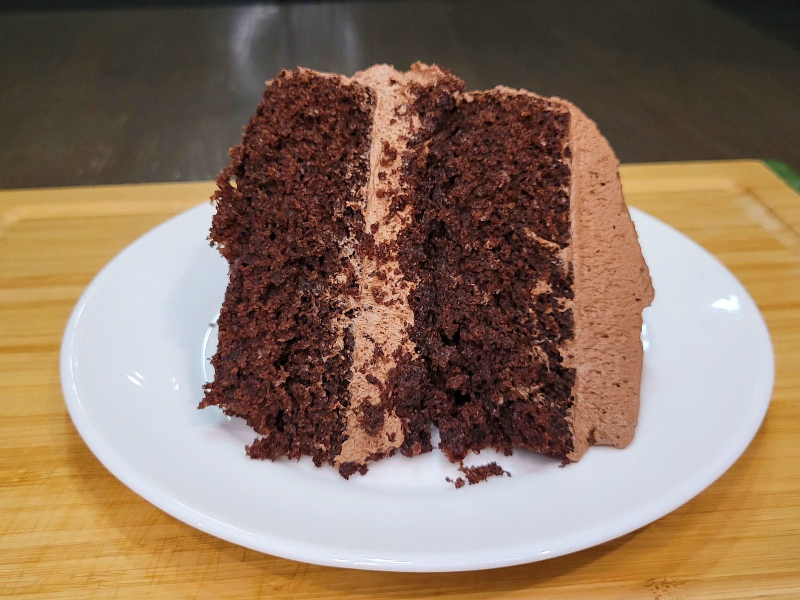 A slice of Chocolate Cake Made With Fresh Milled Flour iced with chocolate buttercream sitting on a white plate.
