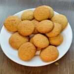 a round white plate on a wooden table that is filled with baked crispy vanilla wafers made with fresh milled flour