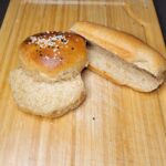 a homemade hamburger bun sliced and a homemade hot dog bun sliced sitting next to each other on a wooden cutting board.