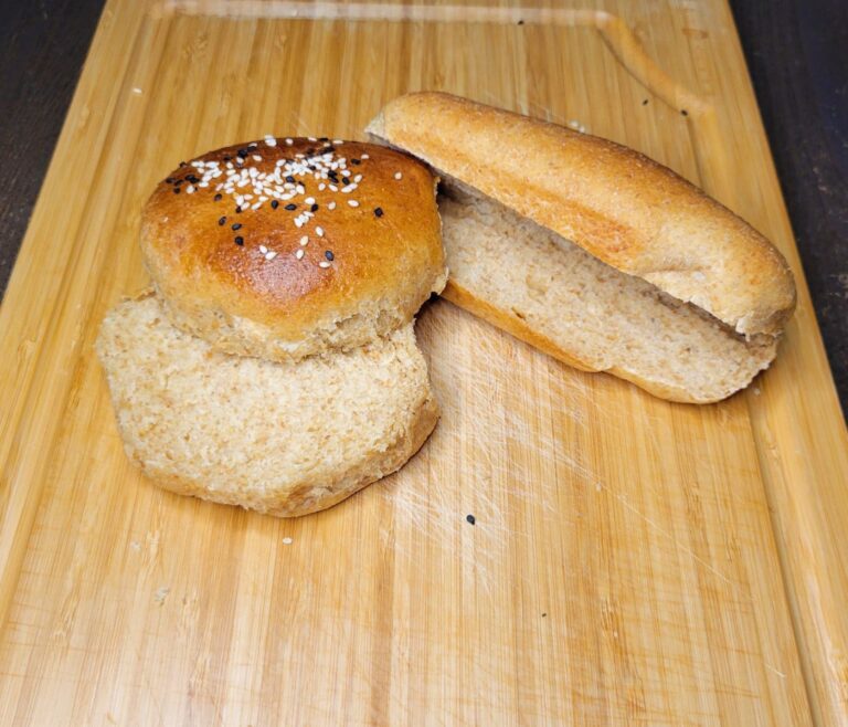 a homemade hamburger bun sliced and a homemade hot dog bun sliced sitting next to each other on a wooden cutting board.