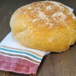 no knead bread loaf made from fresh milled flour sitting on a wooden table with a kitchen towel under it.