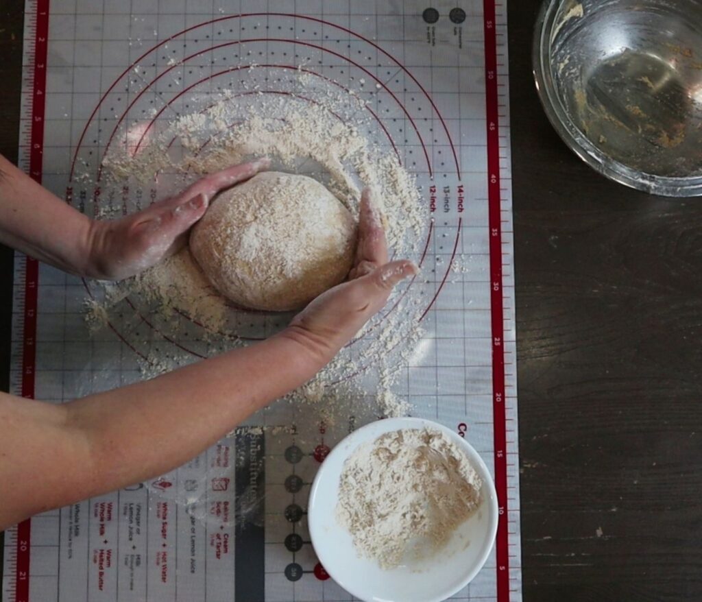 hands shaping no knead bread on a pastry mat with freshly milled flour
