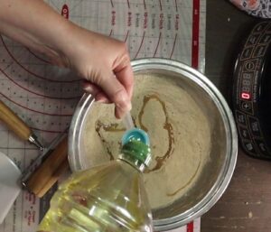 hands using a measuring spoon to pour olive oil into the fresh milled flour to make tortillas