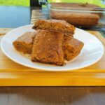 a plate of brown butter chewy blondies made with fresh milled flour on a bamboo cutting board. in front of a glass baking pan with the rest of the blondies.