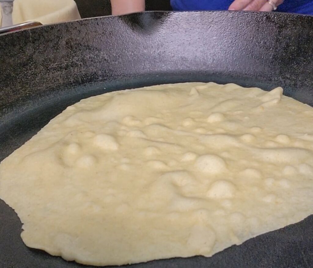 bubbling on the first side of a fresh milled flour tortilla in a cast iron skillet