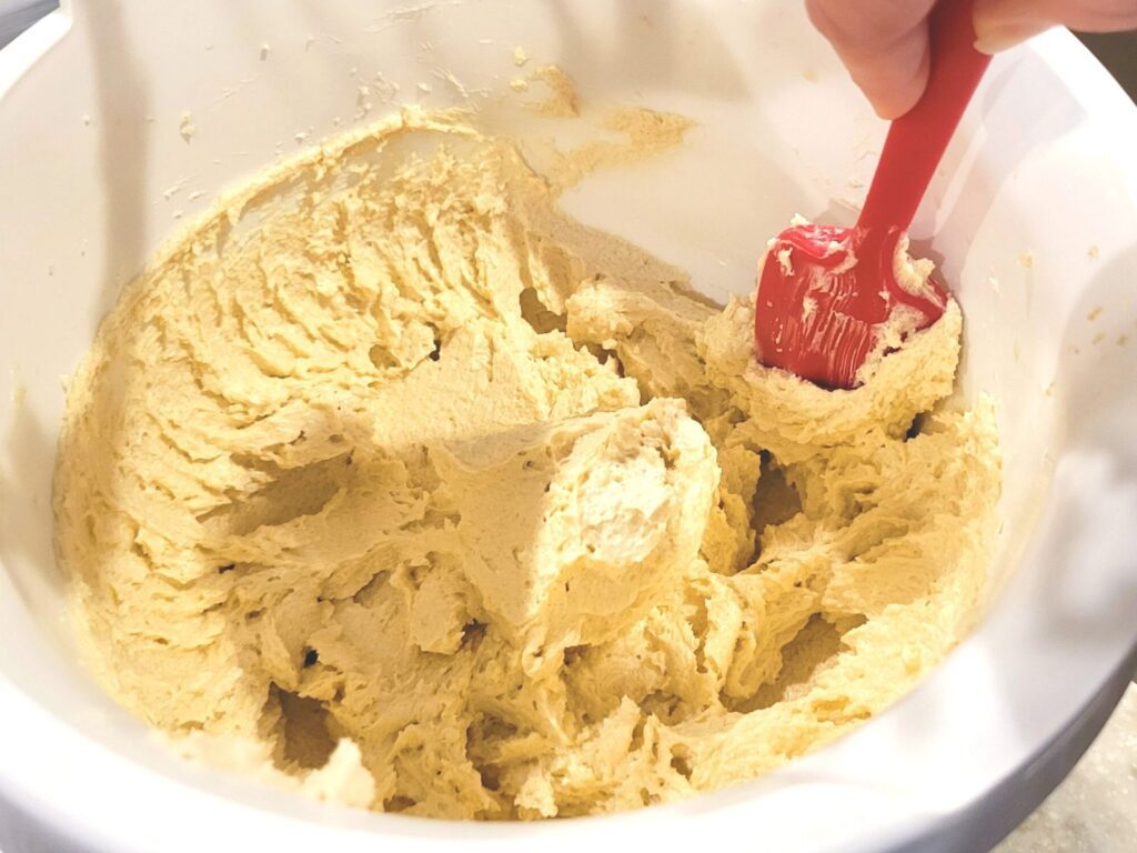 hand stirring creamed butter and sugar with a red spatula in a white mixing bowl