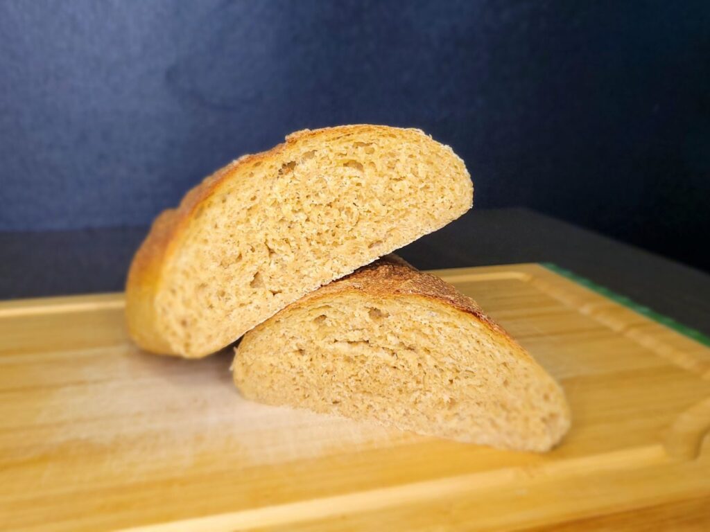 a loaf of crusty french bread sliced in half with one side propped up on the other side. showing the inside crumb of the bread. sitting on a wooden cutting board