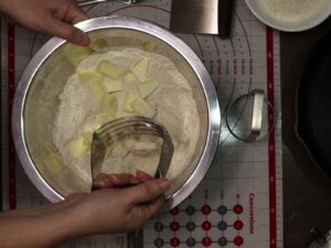 hand cutting cold butter into fresh milled flour biscuit mixture with a pastry cutter