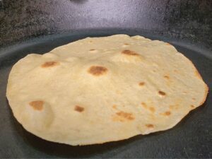 a fresh milled flour tortilla puffing up in a cast iron skillet.