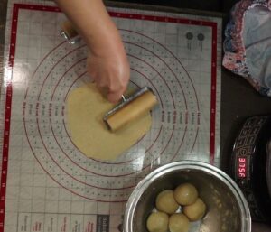 hands using a mini roller to roll out fresh milled flour tortilla dough on a mat with measurement markings.