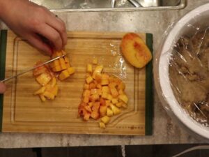hands using a knife to cut a fresh peach into small pieces.