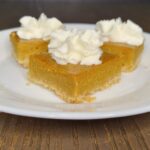 three pumpkin pie bars made with fresh milled flour, topped with a bit of whipped cream and sitting on a white plate.